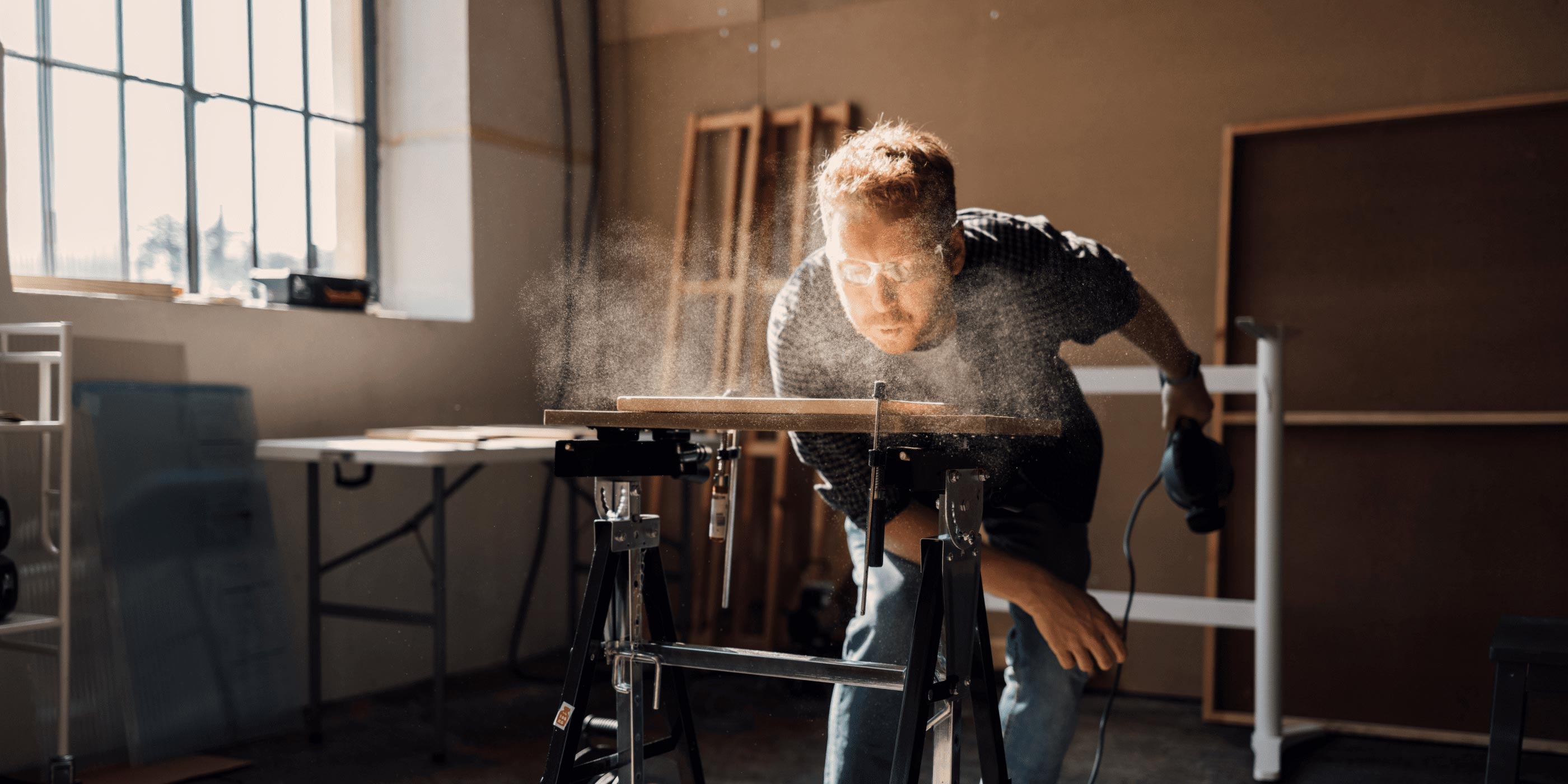 Man blowing away sawdust while working in his workshop