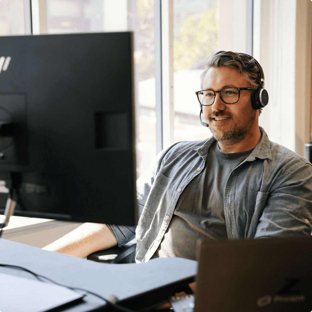 Customer support agent with headset at desk in office.
