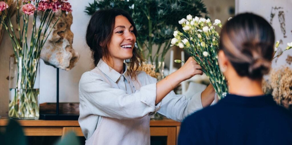 Florist arranging a bouquet of white flowers in a stylish flower shop with greenery and floral arrangements in the background – small business customer experience.