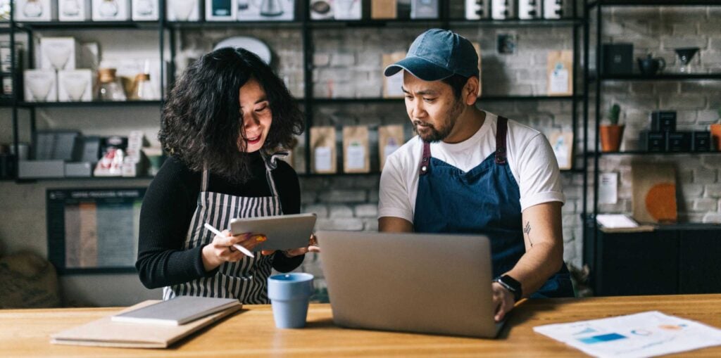 Cafe owners discussing business plans at a counter with a laptop and coffee cup in a stylish cafe interior.