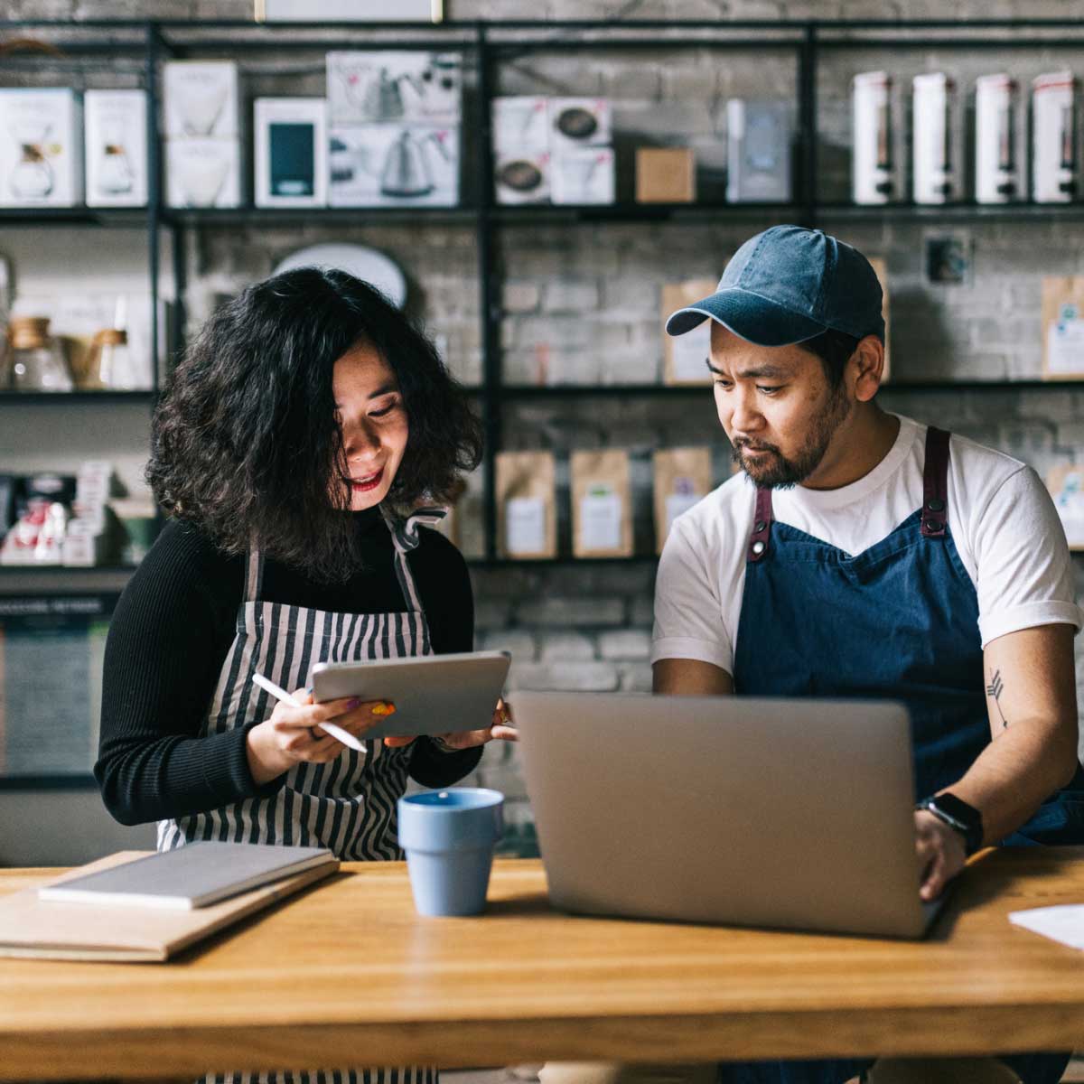 Cafe owners discussing business plans at a counter with a laptop and coffee cup in a stylish cafe interior.