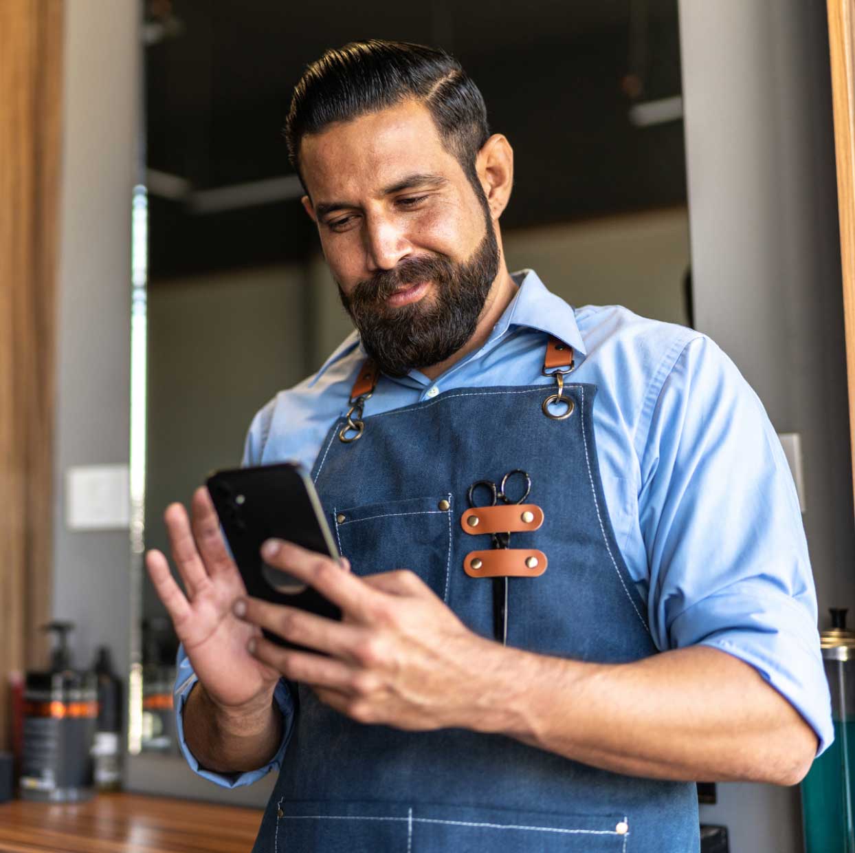 Barber in an apron smiling while using a smartphone