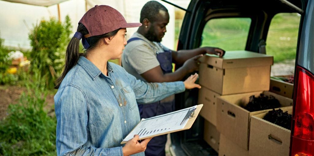 Young farm worker with clipboard directing produce delivery