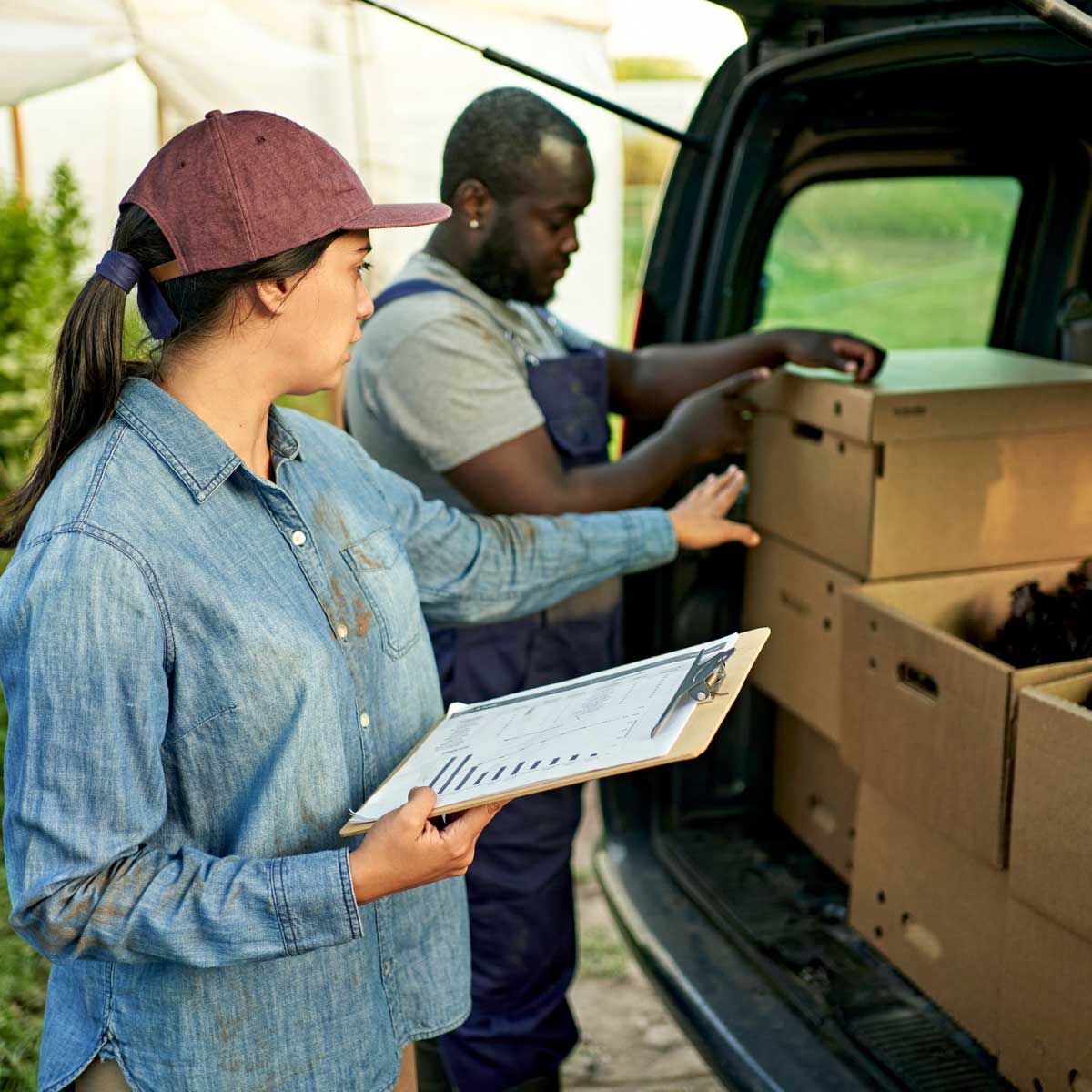 Young farm worker with clipboard directing produce delivery