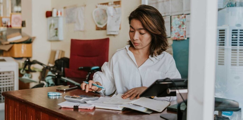 Young business owner does manual accounting using calculator and notepad