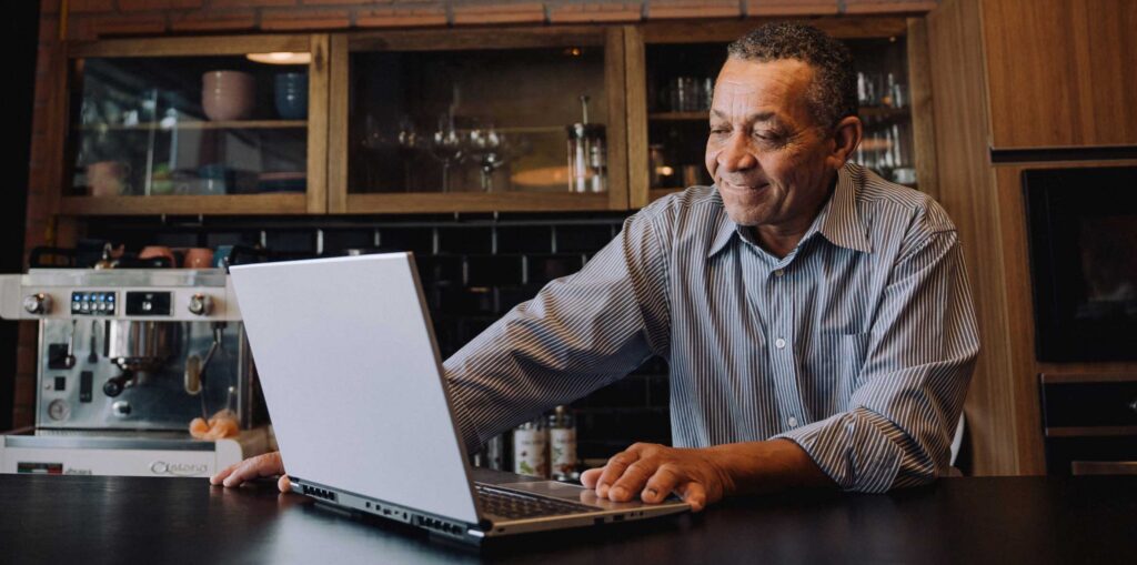 Person working on a laptop at a kitchen counter, with wooden cabinetry and a coffee machine behind them.