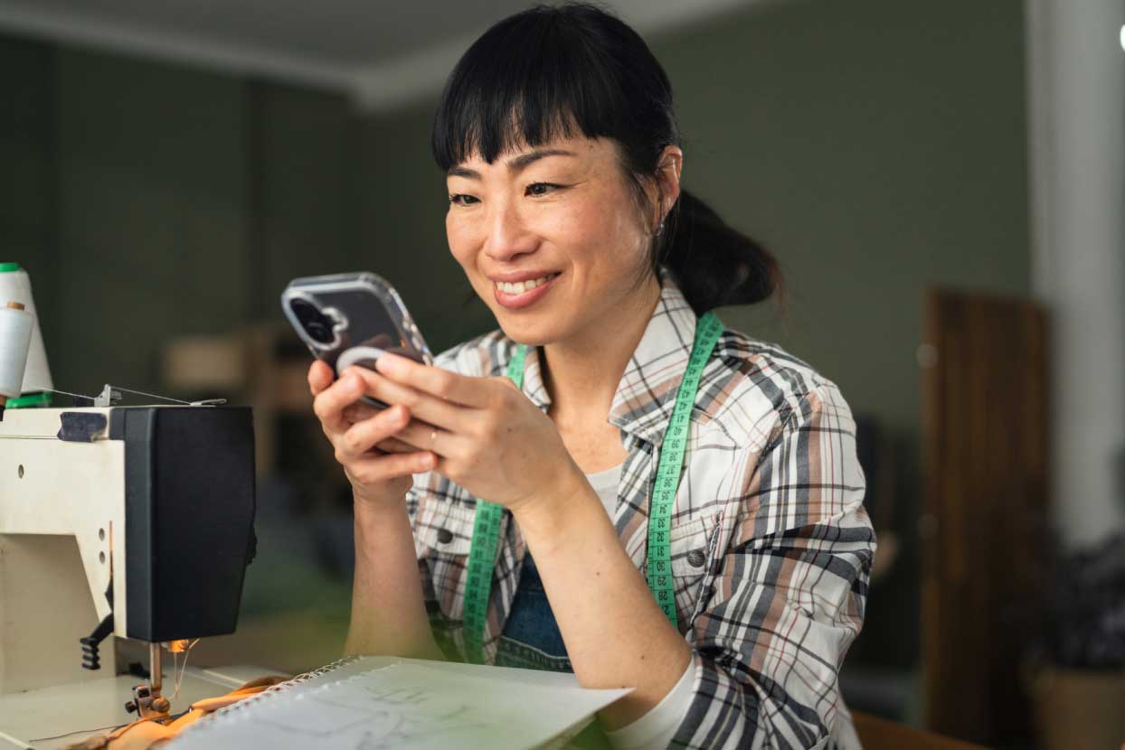 Young Asian woman looking at phone at sewing station