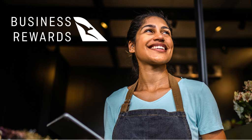 Hospitality worker holding a tablet, with Qantas Points logo displayed in the background.