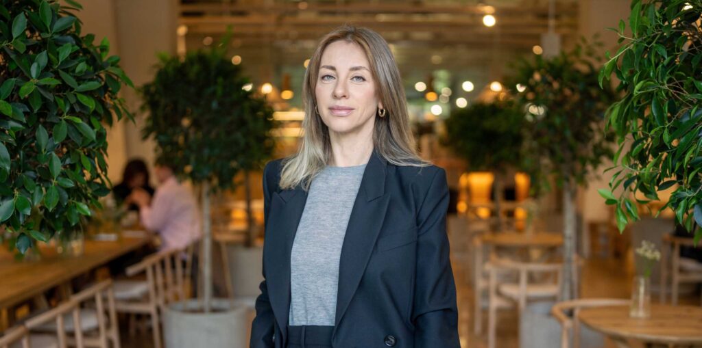 Businesslike confident woman in suit with laptop in hand standing in hall restaurant looks at camera stock photo