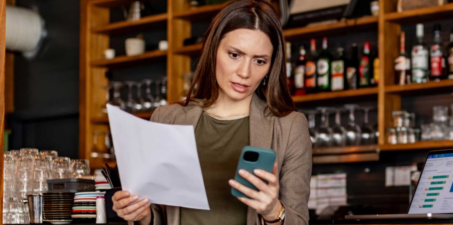 Concerned Small Business Owner Reviewing Financial Reports On Phone At Rustic Bar Counter stock photo